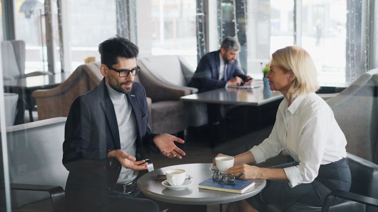 Professional colleagues discuss work over coffee in a contemporary café setting.